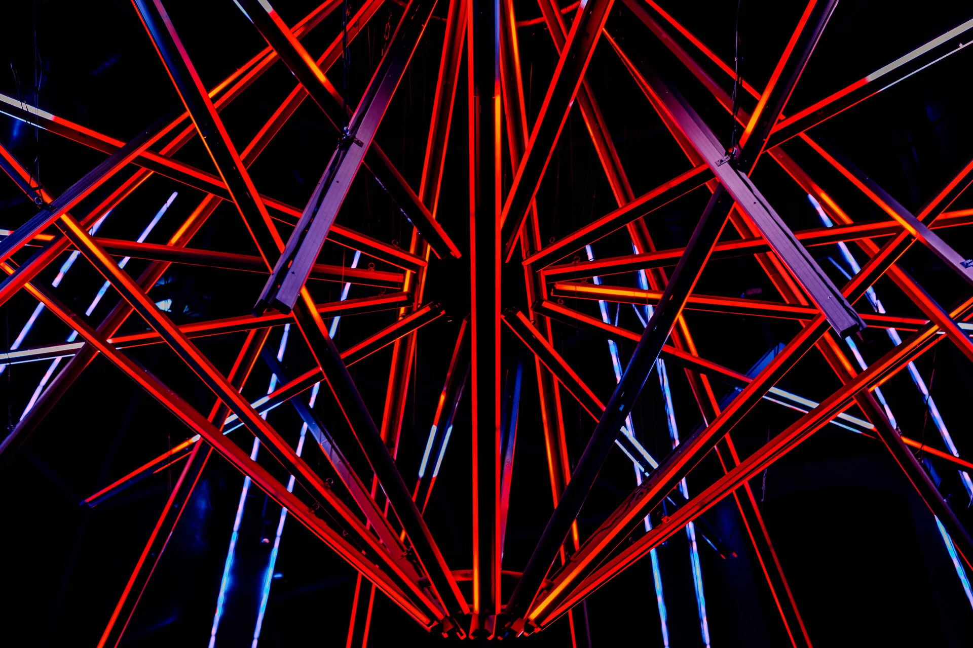 An abstract image of a complex lamp with multiple crossing LEDs that currently are glowing red, with a few glowing with a blueish tint. The lines are crossing in all directions.